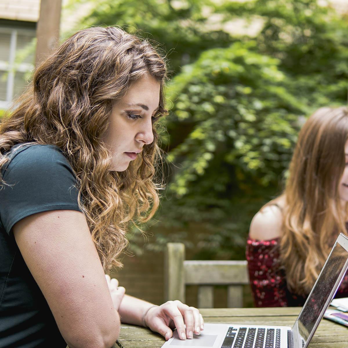 Photo of a student working on her computer at a table outside